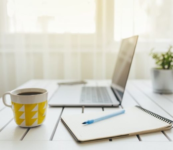 Cup of coffee and laptop on top of a desk.